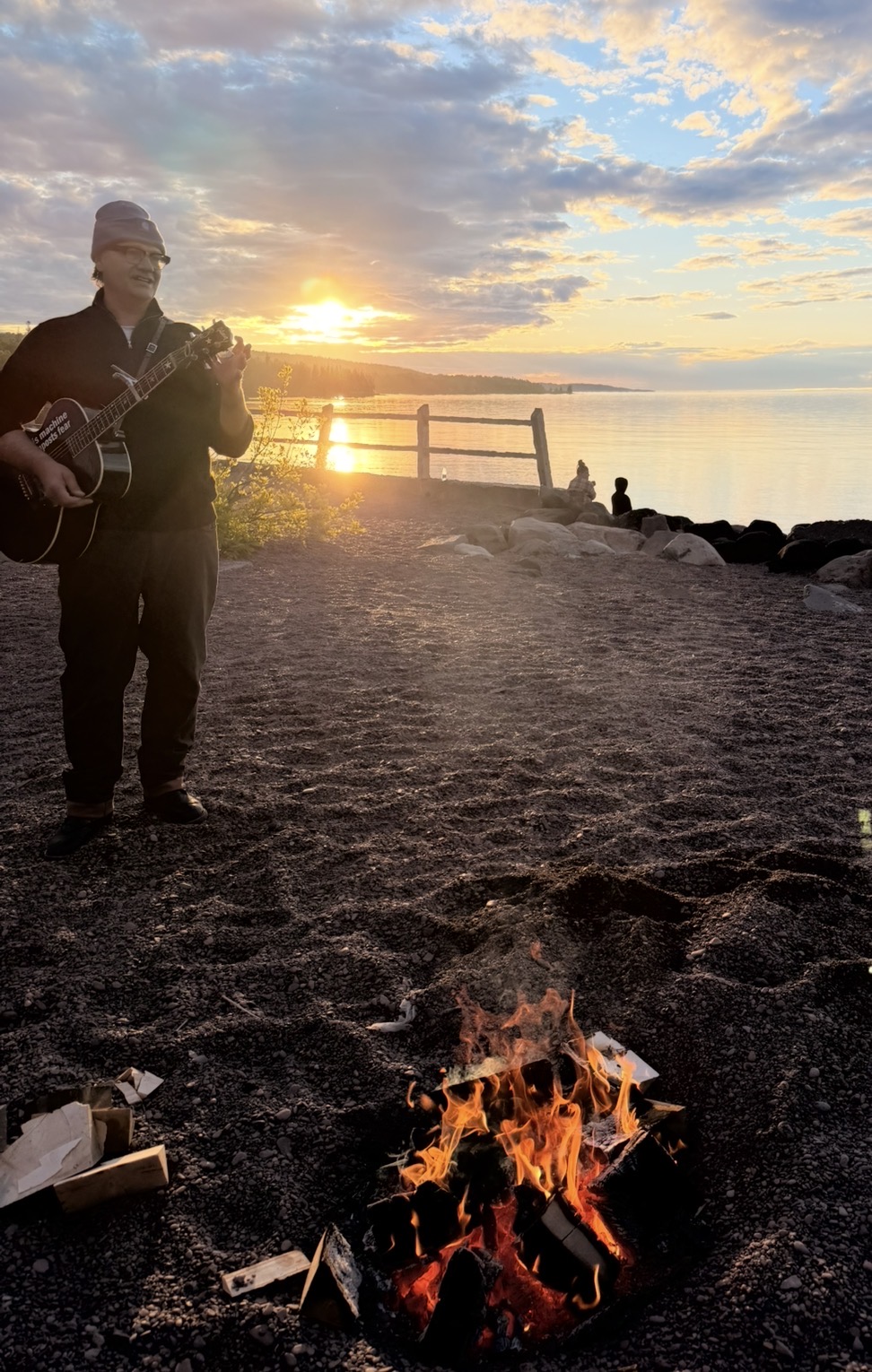 Timothy playing guitar near a fire at sunset
